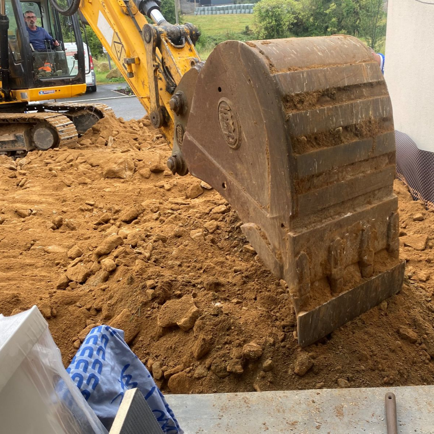 Godet d'excavatrice creusant un sol boueux à côté d'un bâtiment