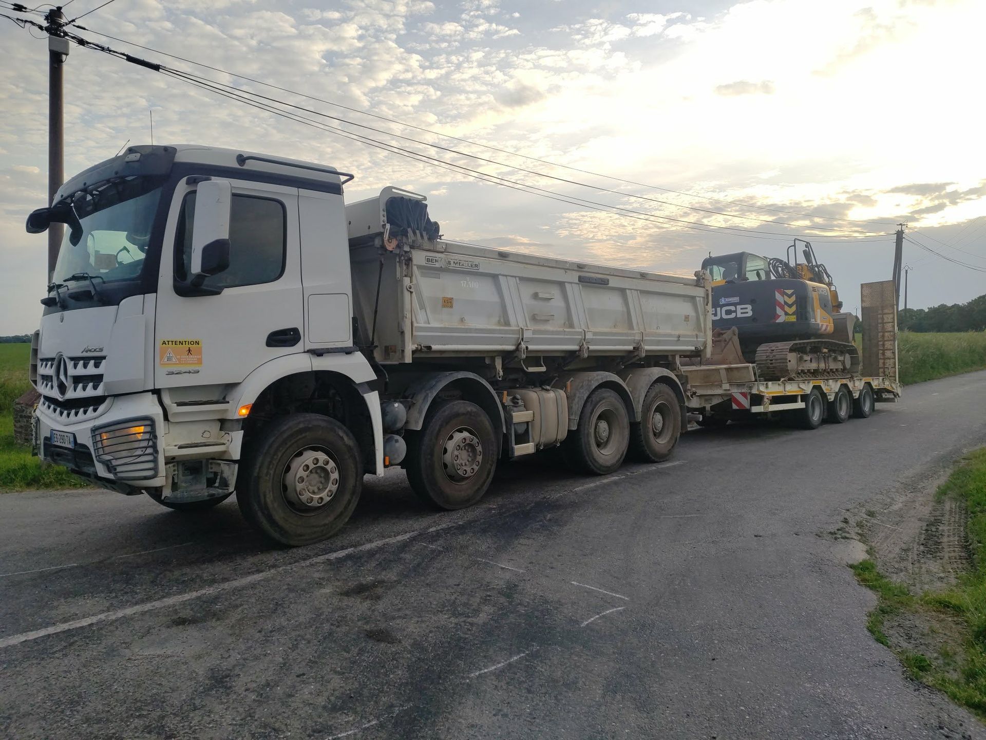 Un camion-benne blanc transporte de la machinerie lourde sur une remorque dans un parking.