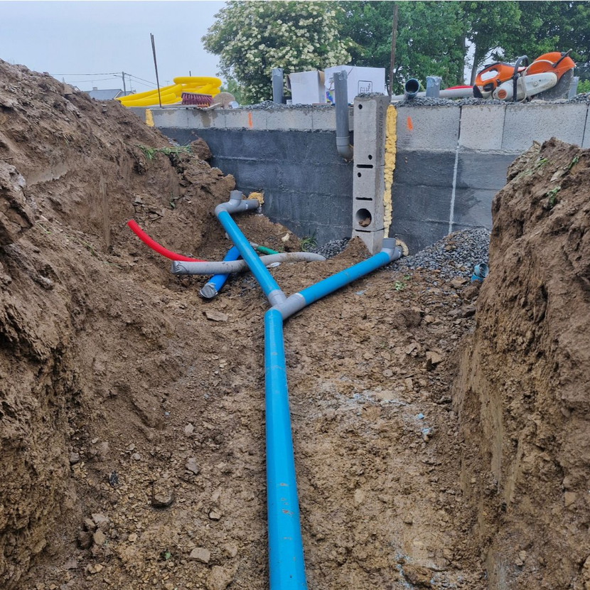 Des tuyaux bleus dans une tranchée creusée à côté d'un mur de soutènement en béton sur un chantier de construction.