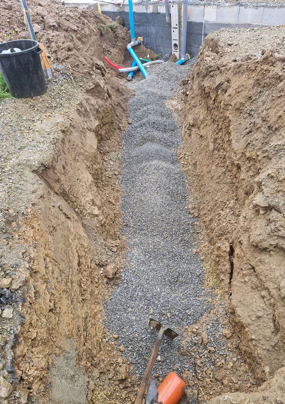 Tranchée avec lit de drainage en gravier et canalisations apparentes sur un chantier de construction