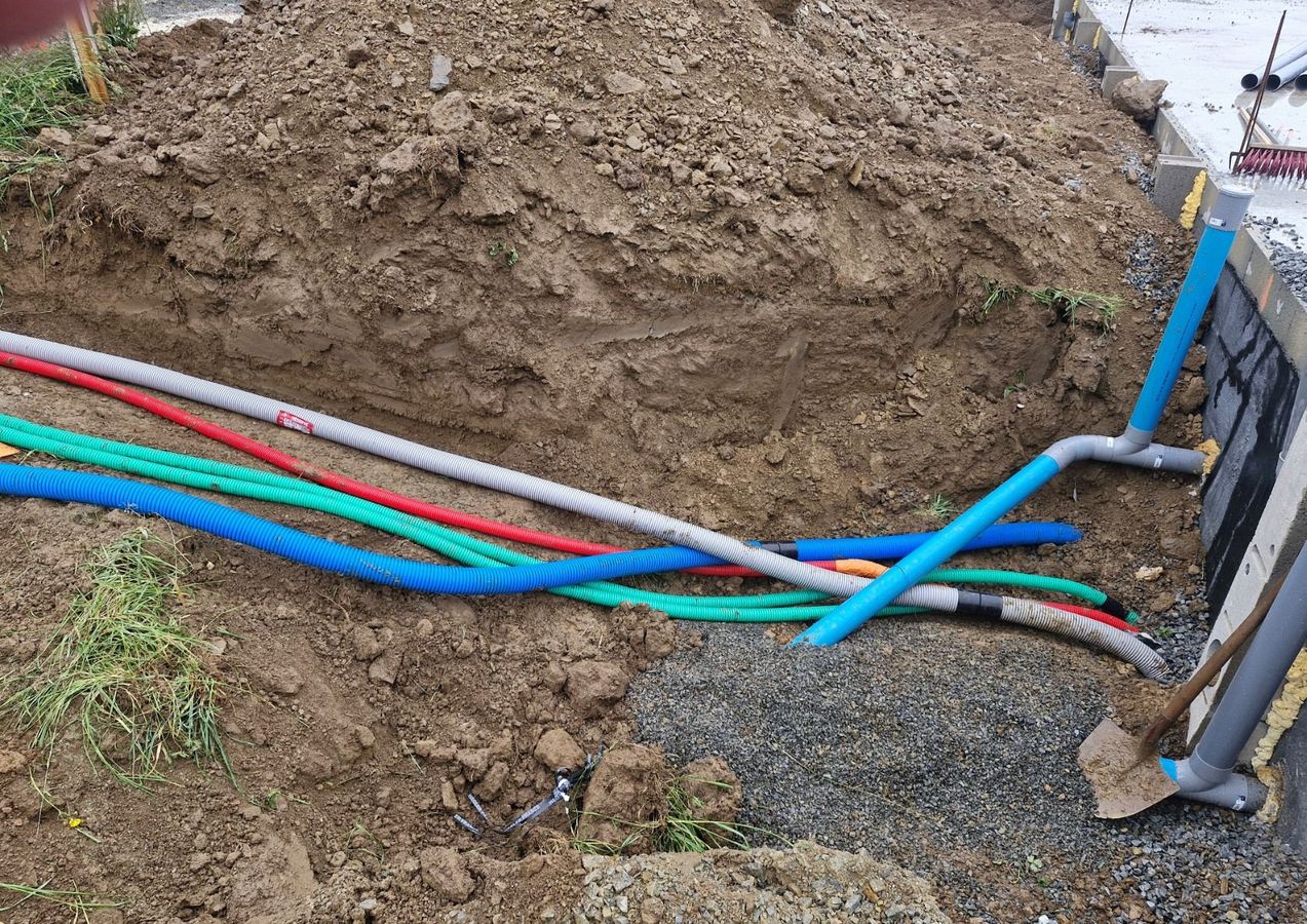 Des tuyaux d'égout colorés apparaissent dans une tranchée de terre, à côté d'un monticule de terre et d'une pelle.