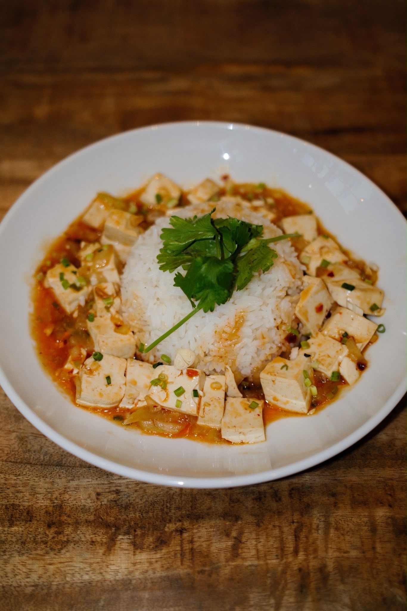 Assiette de riz au tofu dans une sauce au curry rouge, garnie de coriandre, sur une table en bois