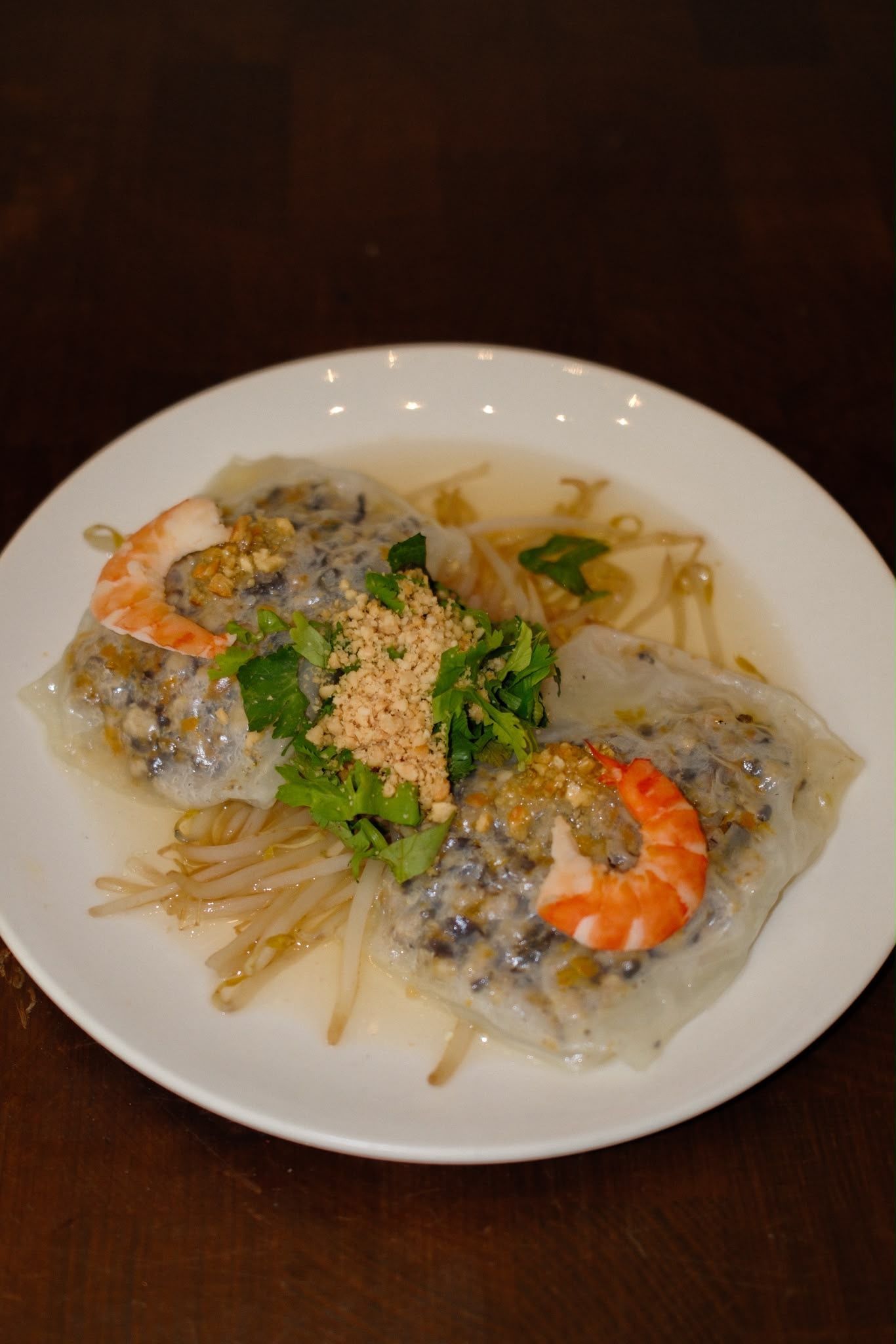 Assiette blanche de nouilles aux crevettes, herbes et cacahuètes concassées sur une table sombre