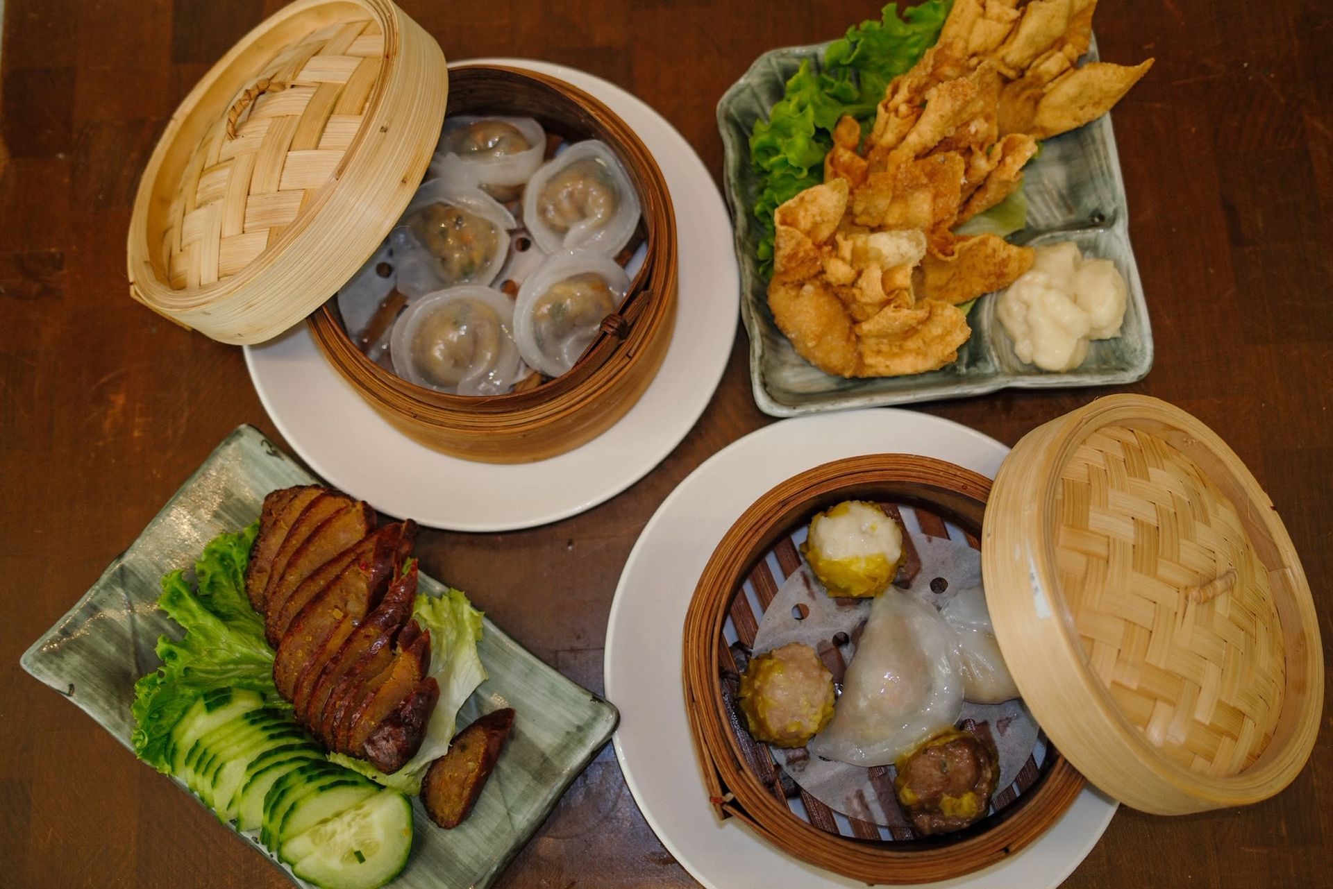 Trois paniers de dim sum disposés sur une table, contenant des raviolis, des petits pains et des rouleaux frits, le tout sur un lit de verdure.