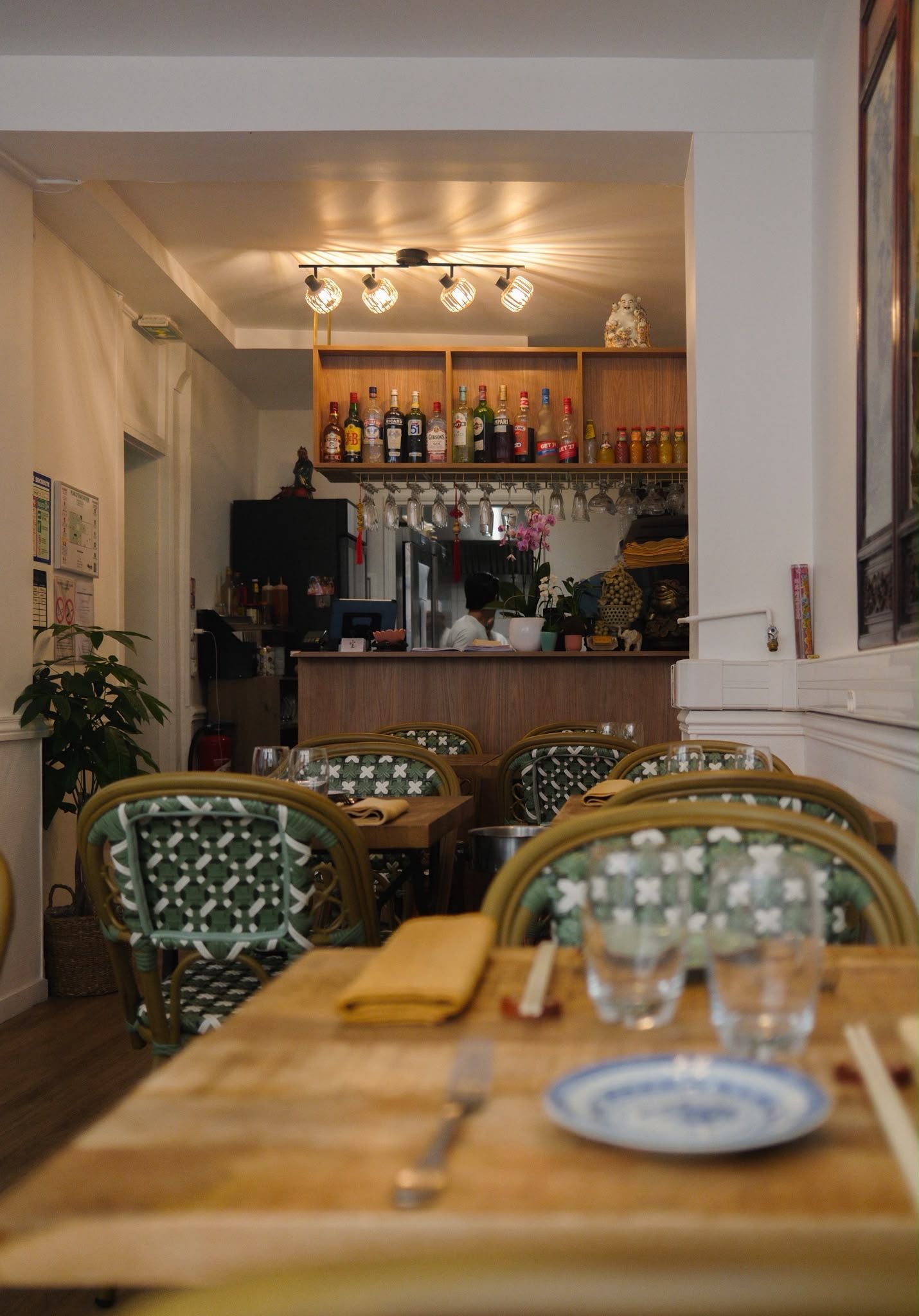 Intérieur de café chaleureux avec chaises à motifs, tables en bois et étagères de bouteilles au fond.
