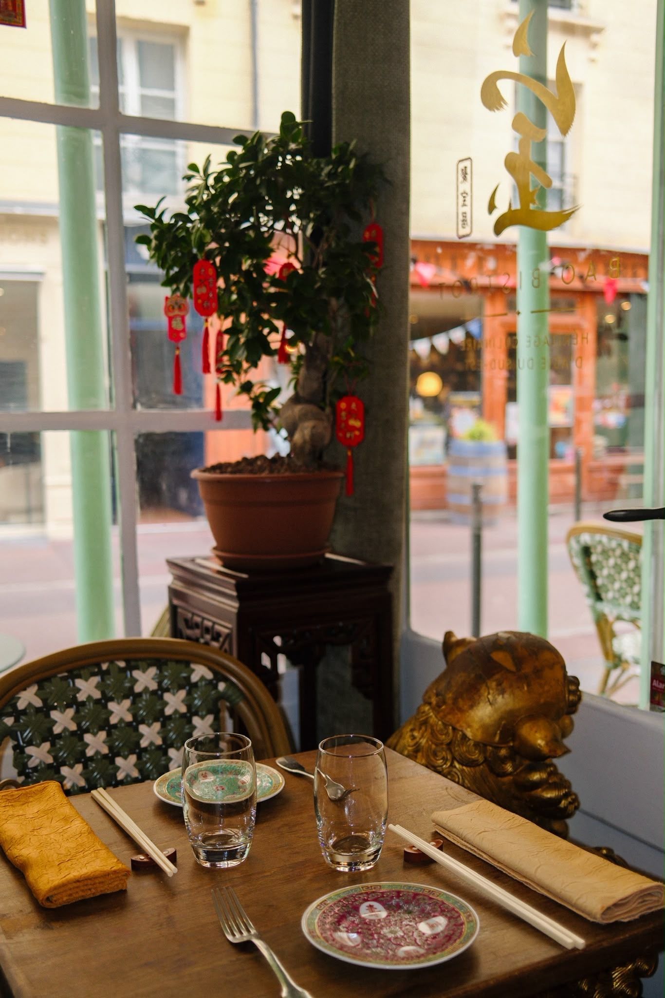 Table de restaurant près d'une fenêtre avec assiettes, baguettes, tasses à thé et une plante en pot sur un support