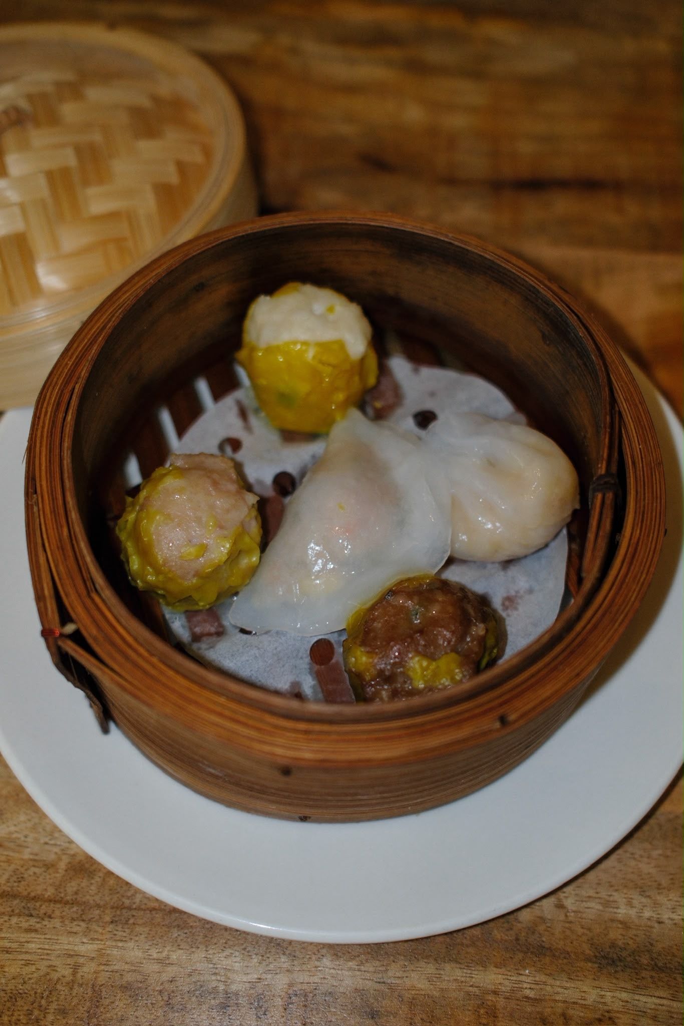 Des raviolis cuits à la vapeur dans un panier en bambou sur une assiette blanche, nappés d'une sauce crémeuse.