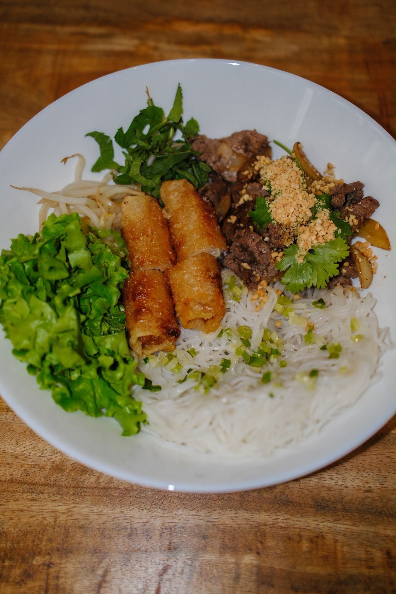 Assiette de nouilles de riz avec rouleaux de printemps, légumes verts et herbes aromatiques sur une table en bois