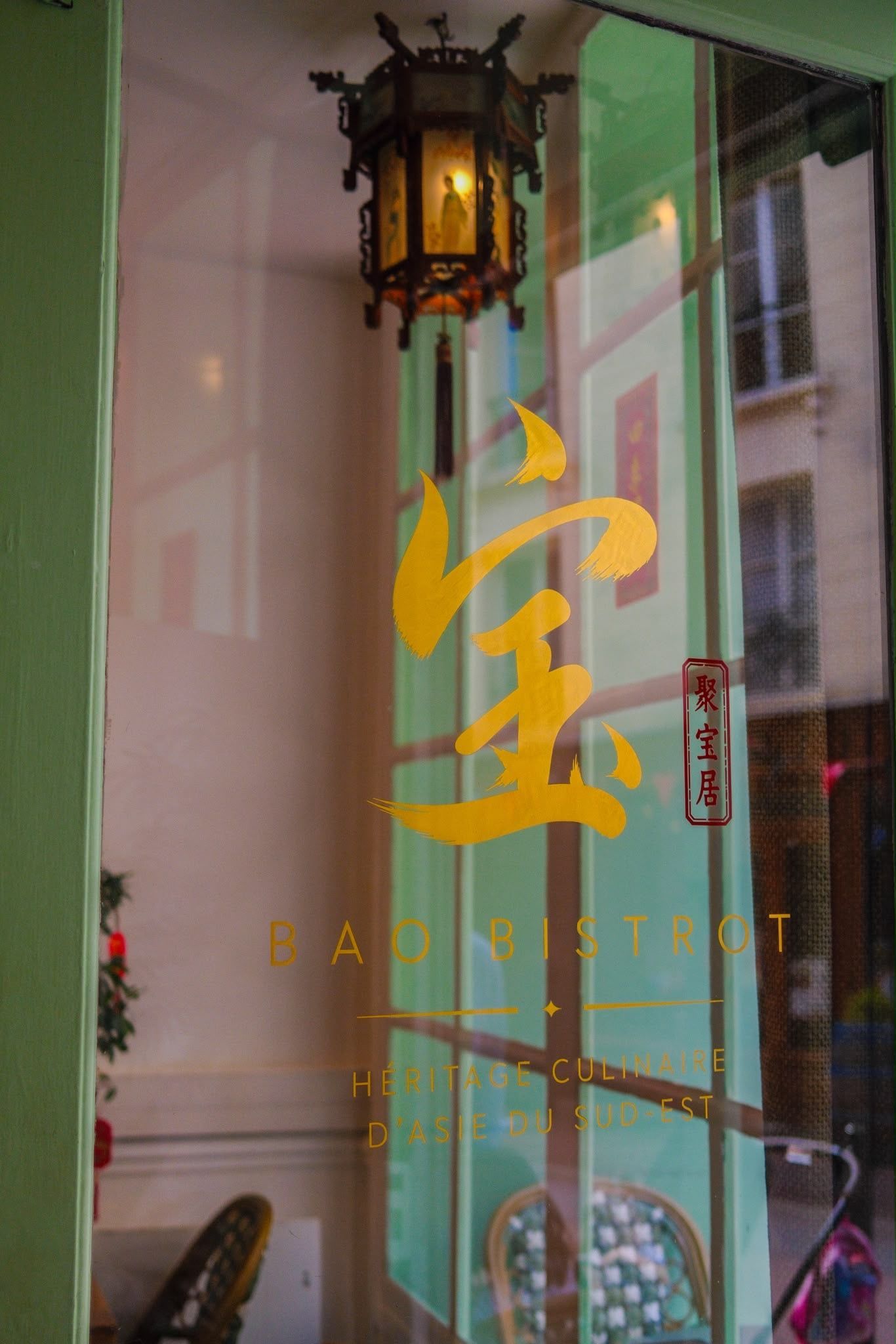 Porte vitrée de magasin avec inscriptions chinoises dorées et lanterne suspendue se reflétant dans la vitre.