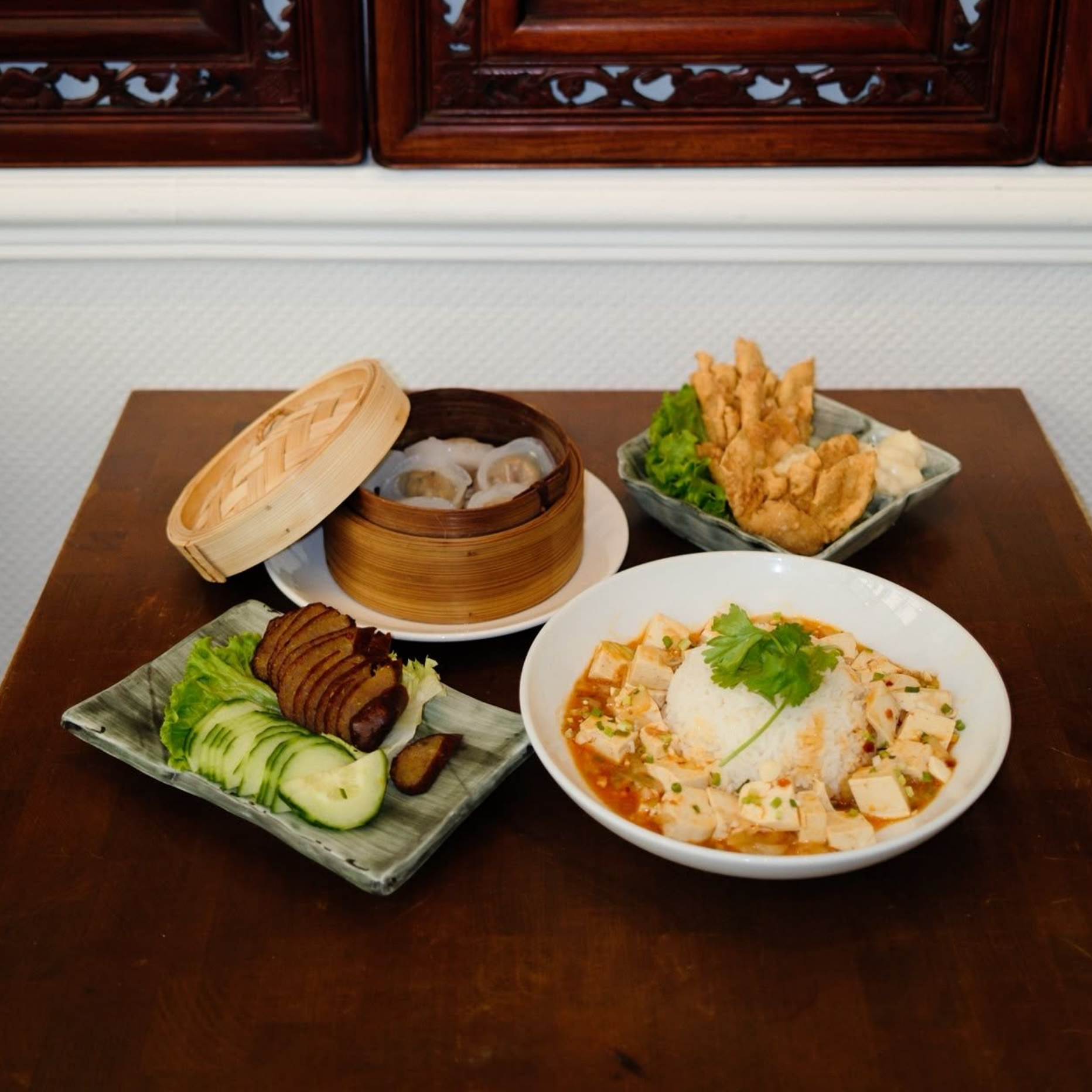 Repas asiatique servi sur une table en bois avec dim sum, crevettes frites, viande tranchée et un bol de soupe de nouilles