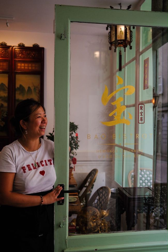 Femme debout près d'une porte vert menthe à l'intérieur d'un café chaleureux, souriante et regardant vers la droite