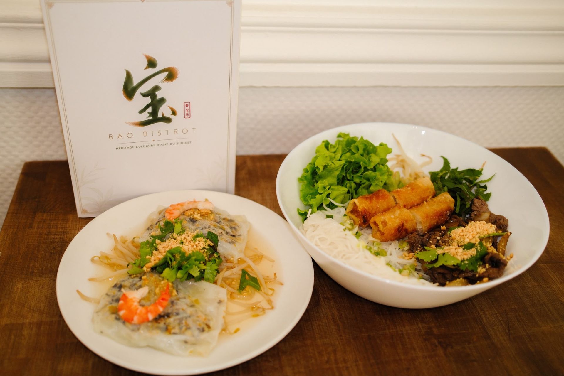 Deux assiettes de nouilles avec des légumes verts sont disposées sur une table à côté d'un présentoir à menus.