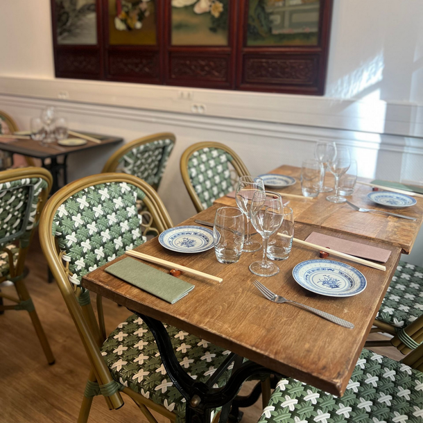 Petite table à manger avec chaises à motifs verts, verres et assiettes bleues et blanches dans une pièce ensoleillée