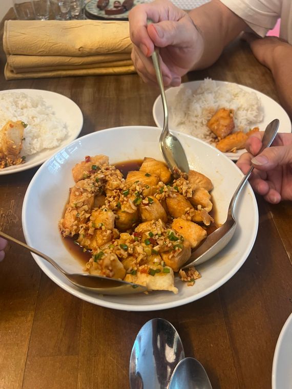 Table de riz servi dans une assiette avec du poulet en sauce, accompagné de couverts et des mains d'une personne qui plongent des cuillères dedans.