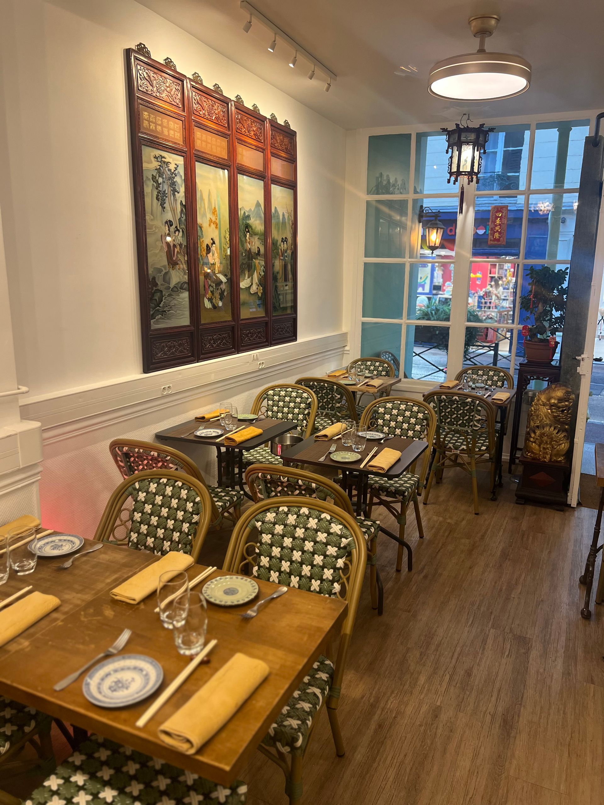 Salle à manger chaleureuse avec tables en bois, chaises à motifs et vue sur la rue à travers les fenêtres de façade