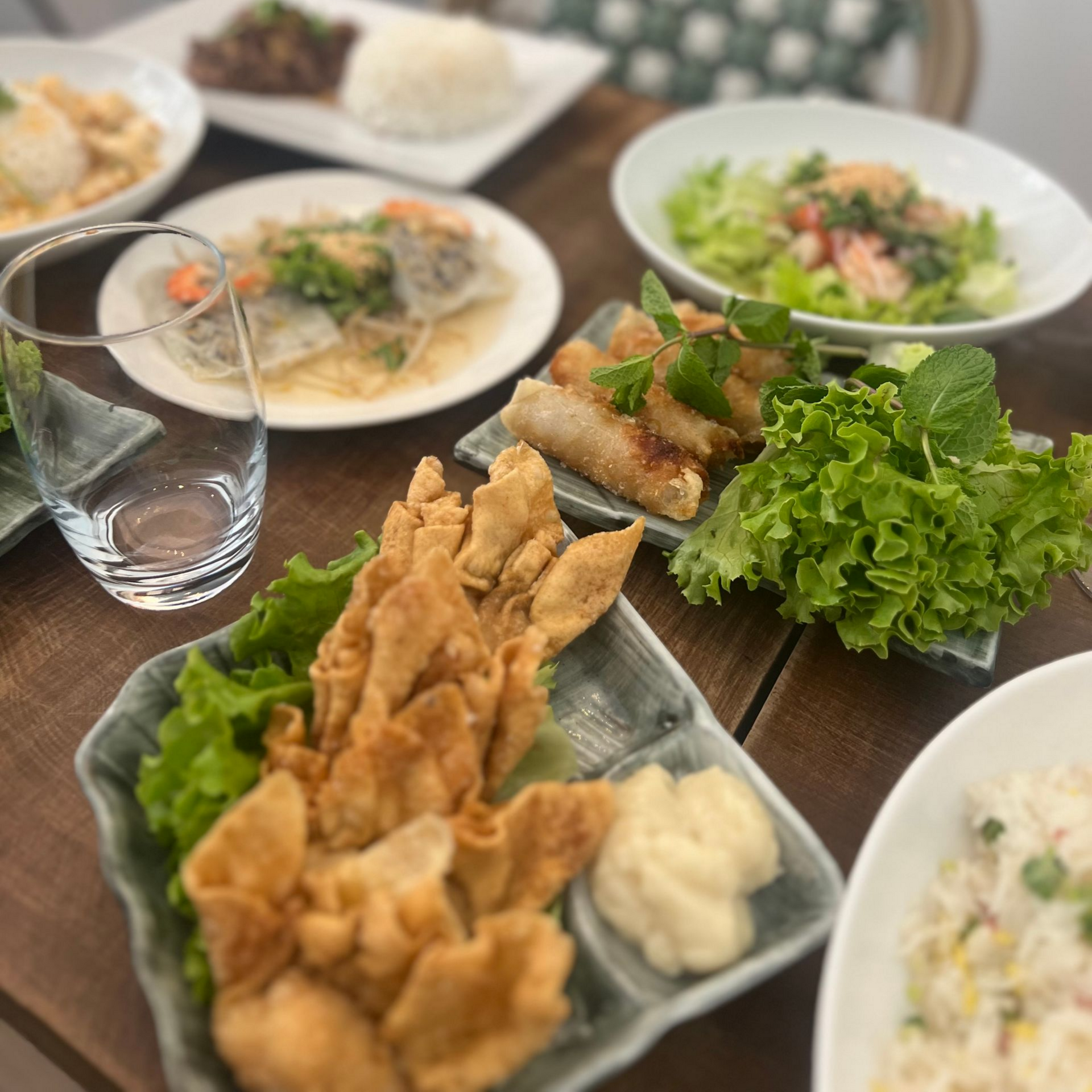 Table garnie de plats variés : beignets frits, salade, riz et un verre d'eau, le tout sur une table en bois.