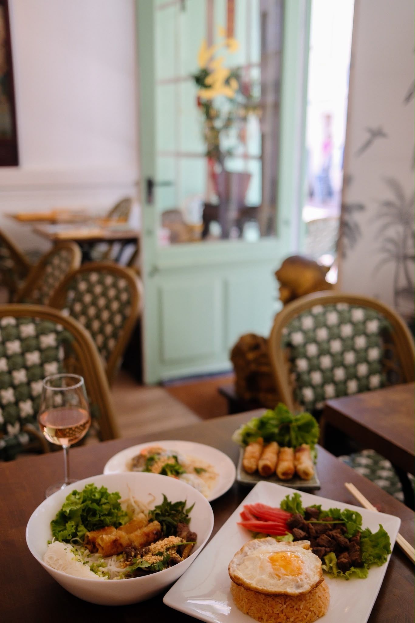 Des assiettes de brunch dressées sur une table de restaurant, avec du vin et un intérieur vert menthe en arrière-plan.