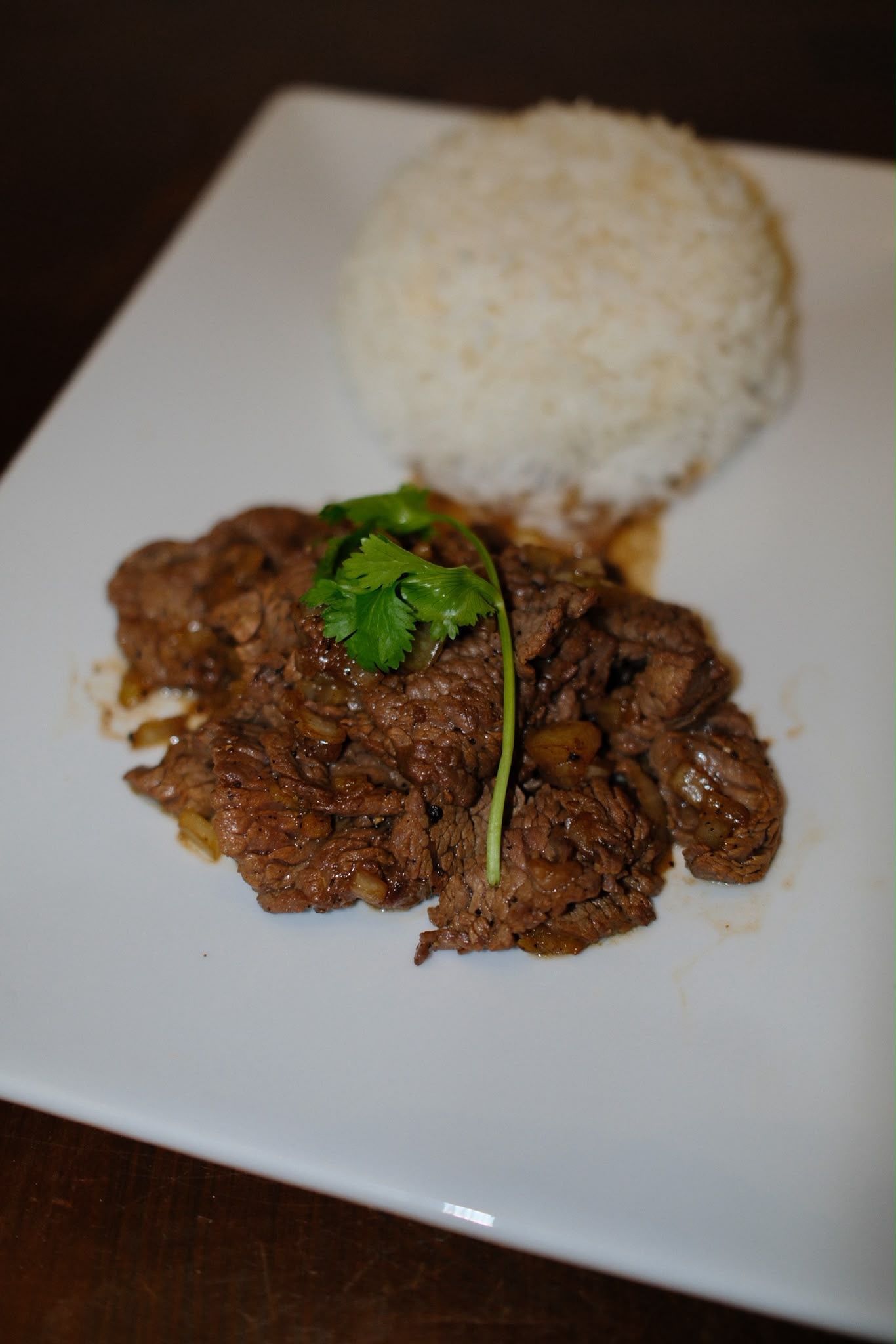 Riz servi dans une assiette blanche avec de la viande dorée et une garniture de persil.