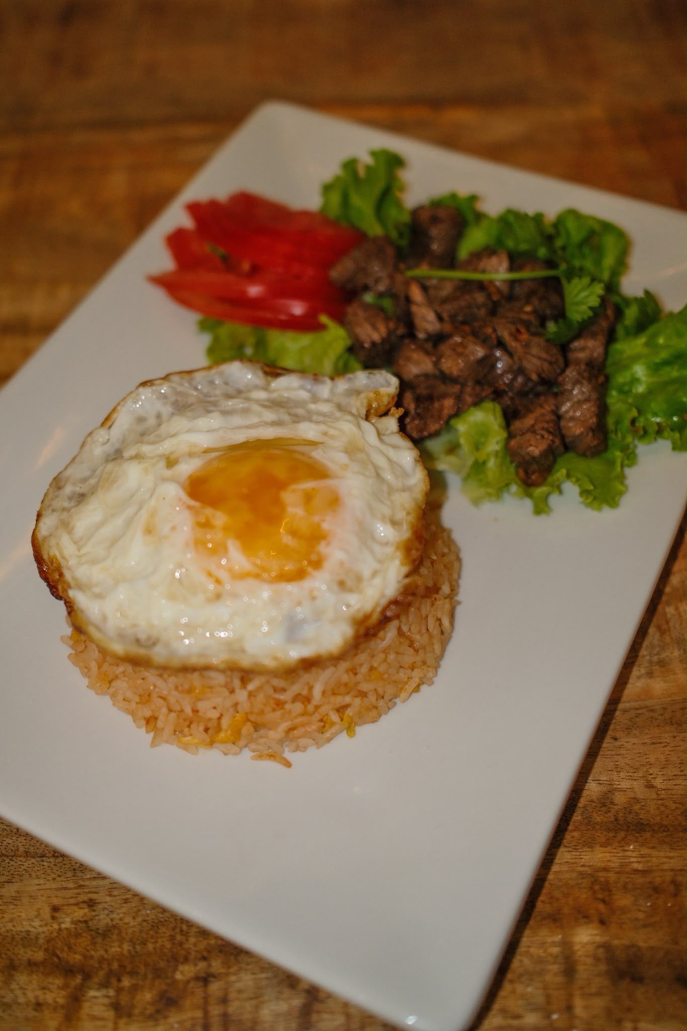 Œuf au plat sur du riz avec de la viande grillée et de la laitue dans une assiette blanche
