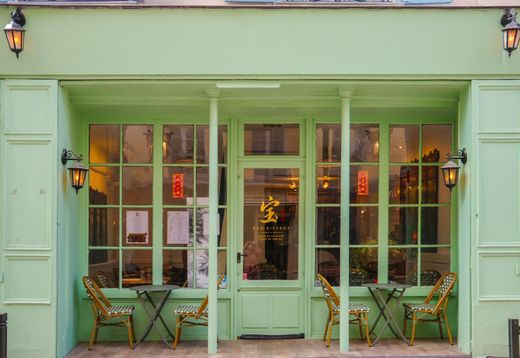 Façade vert pastel avec de grandes fenêtres, tables et chaises de terrasse à l'extérieur