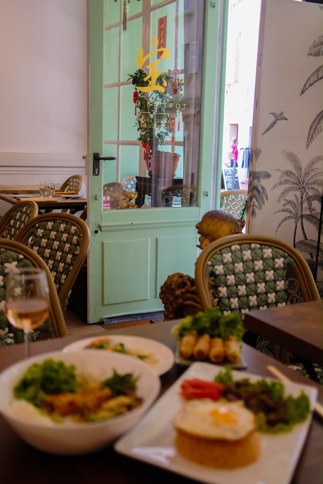 Table de restaurant avec salades et toasts devant une porte vert pastel et des chaises à motifs.