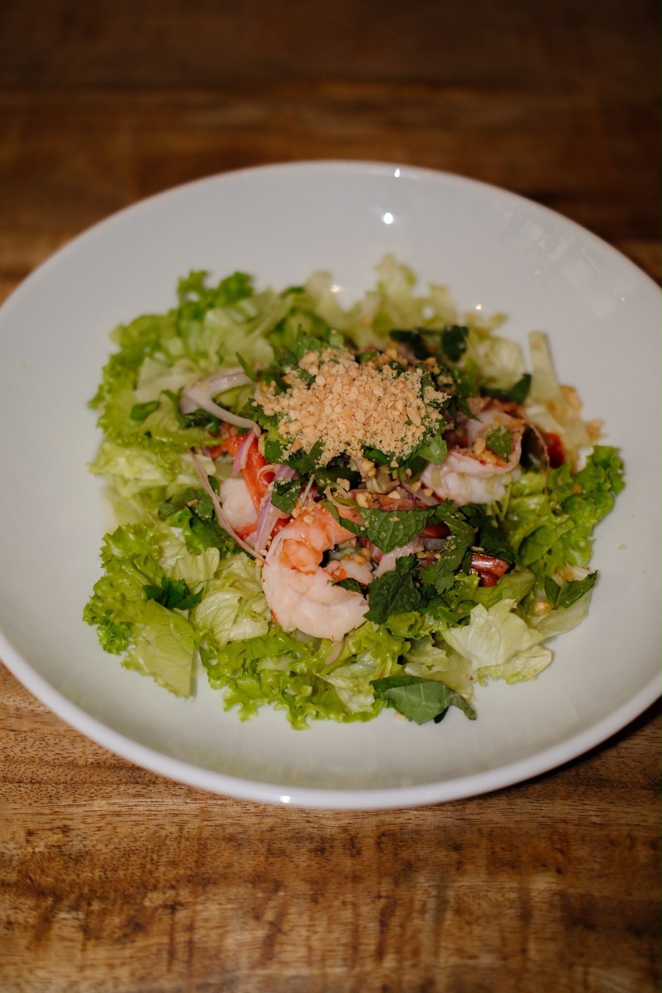 Salade de crevettes aux graines de sésame dans un bol blanc sur une table en bois