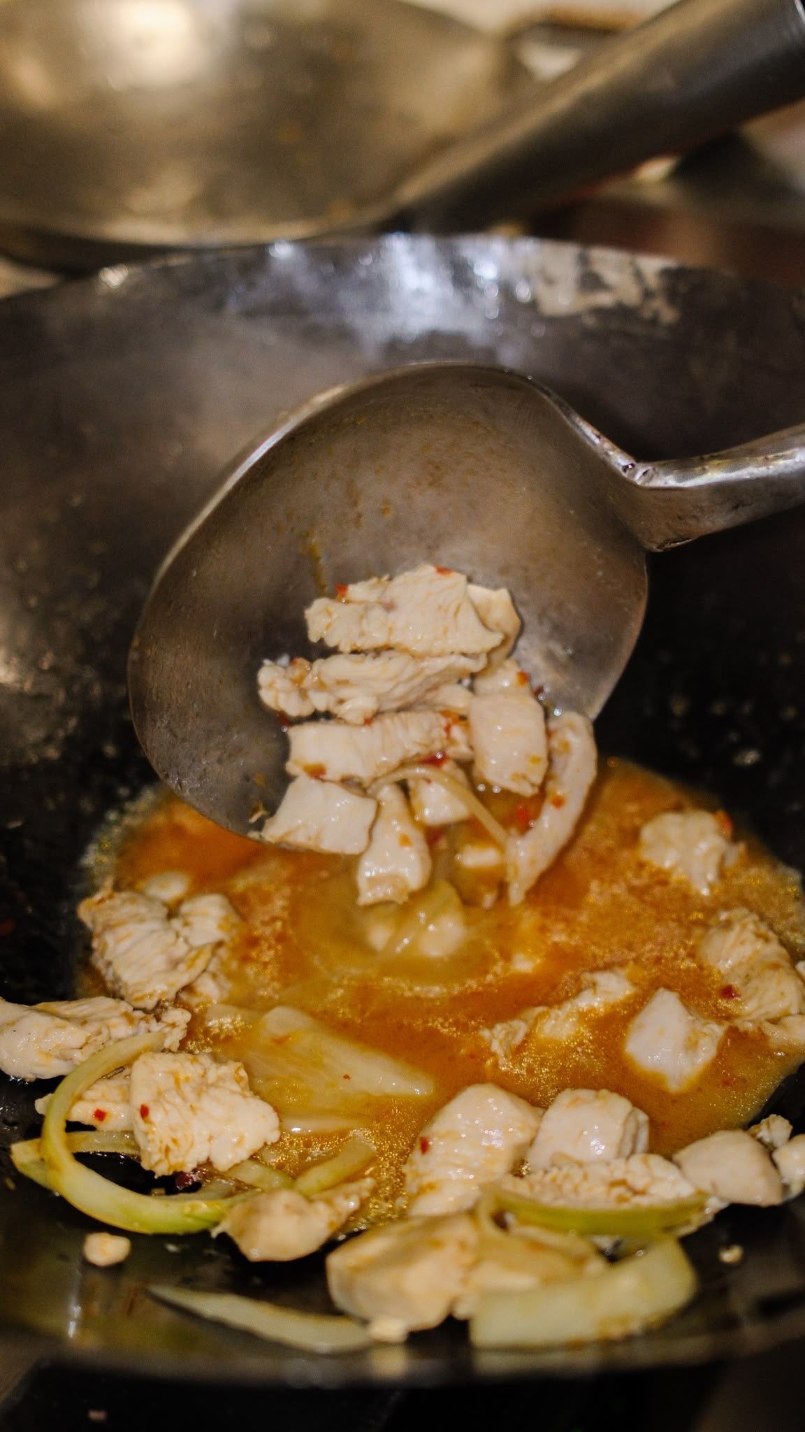 Une cuillère retire de la viande hachée d'un wok contenant une sauce à l'orange et des légumes coupés en tranches.
