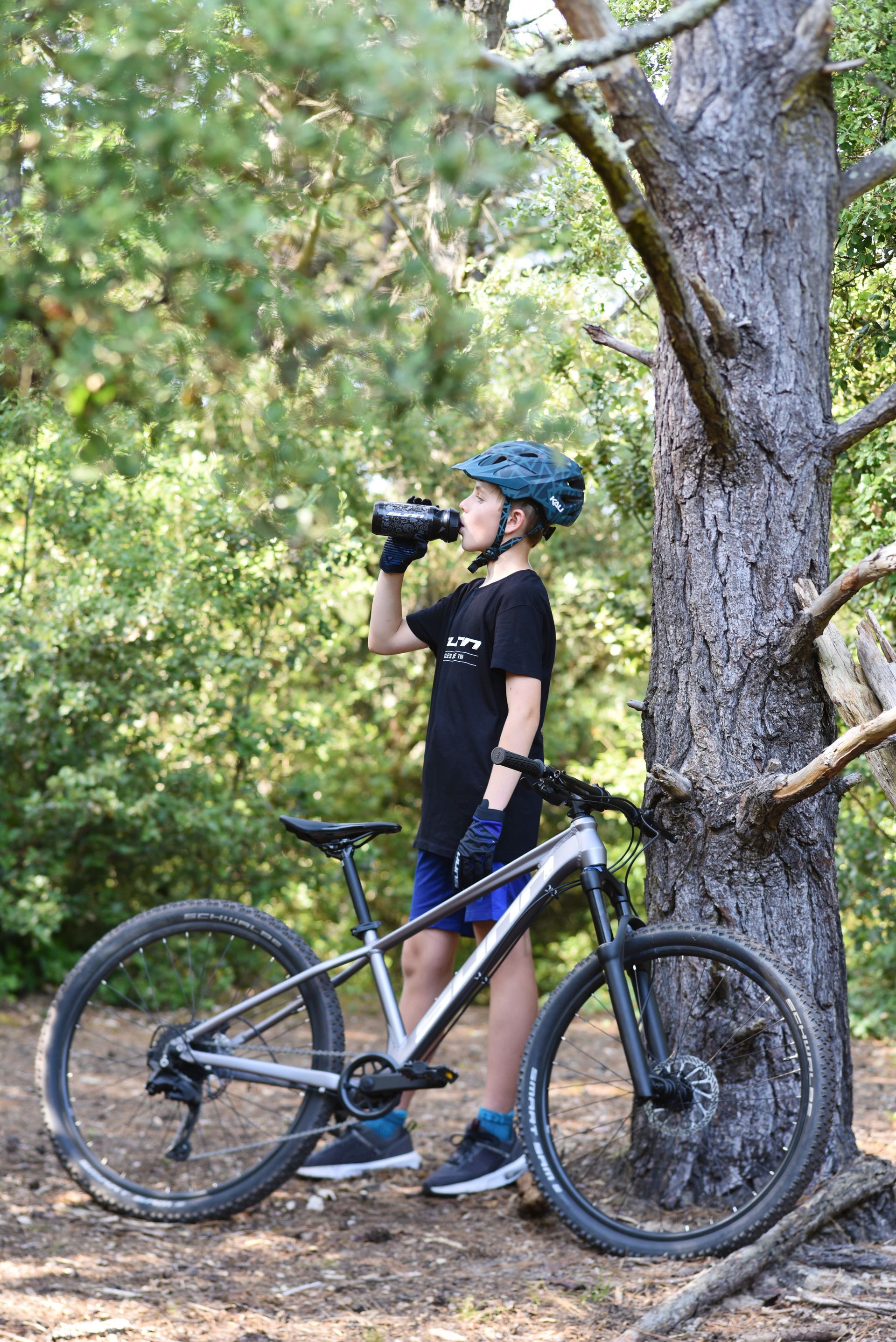 Un enfant boit à la gourde devant un vélo junior gris