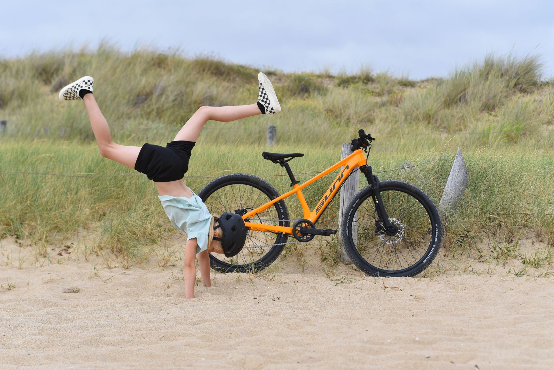 Un enfant fait une cabriole devant vélo orange pour grands enfants