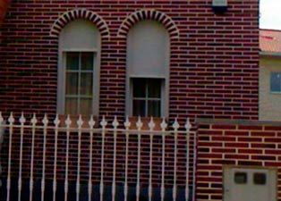 Un edificio de ladrillo con ventanas arqueadas y una valla blanca.