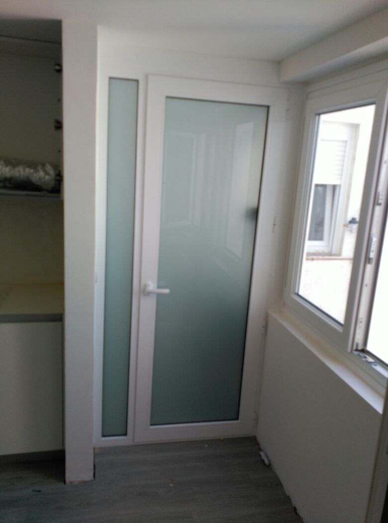 Una puerta blanca con vidrio esmerilado está en una habitación al lado de una ventana.