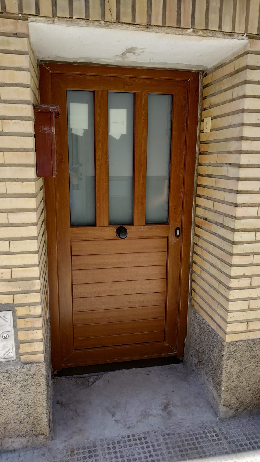 Una puerta de madera con tres ventanas está en un edificio de ladrillo.