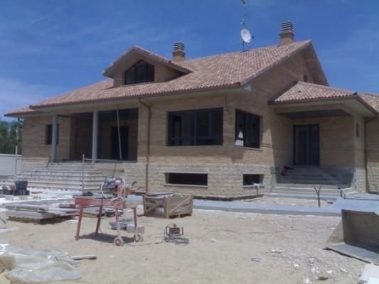 Se está construyendo una gran casa de ladrillo con techo de tejas.