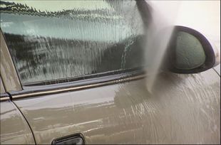 El coche está siendo lavado con abundante espuma de jabón que cubre la puerta y el espejo lateral.