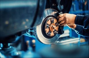 Un mecánico inspecciona un disco de freno de un coche con una llave inglesa en un garaje iluminado con luz azul.