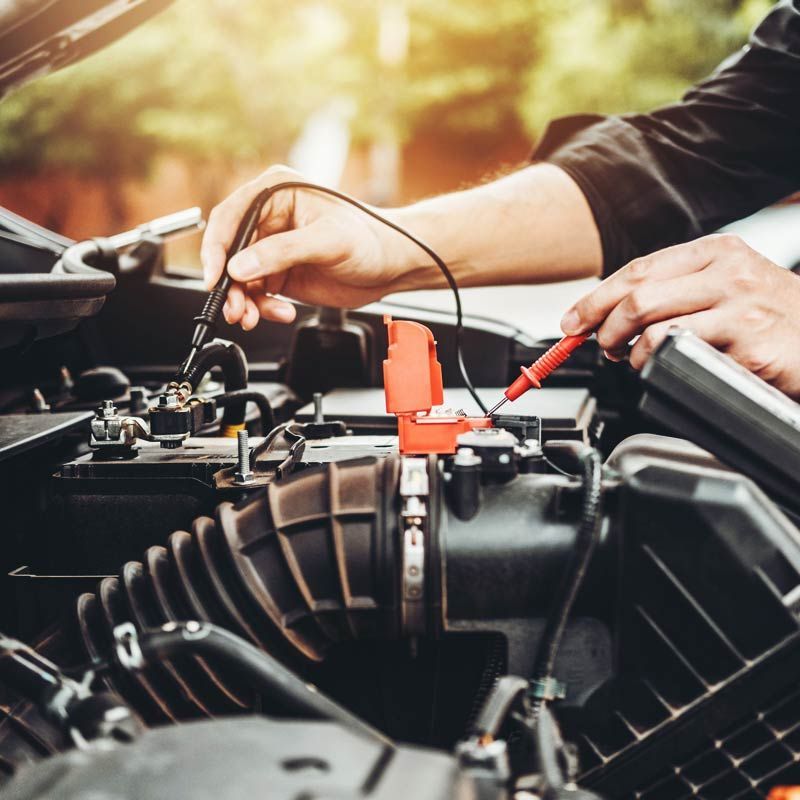 Manos usando cables de arranque en la batería de un coche en el compartimento del motor.