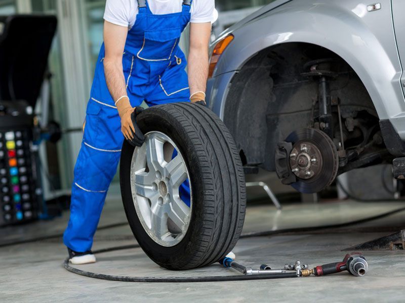 Un mecánico está cambiando un neumático de un coche en un taller de reparación, con las herramientas esparcidas por el suelo.