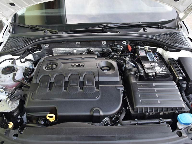 Compartimento del motor del coche con cubierta del motor negra, batería a la derecha y tapa del limpiaparabrisas azul.