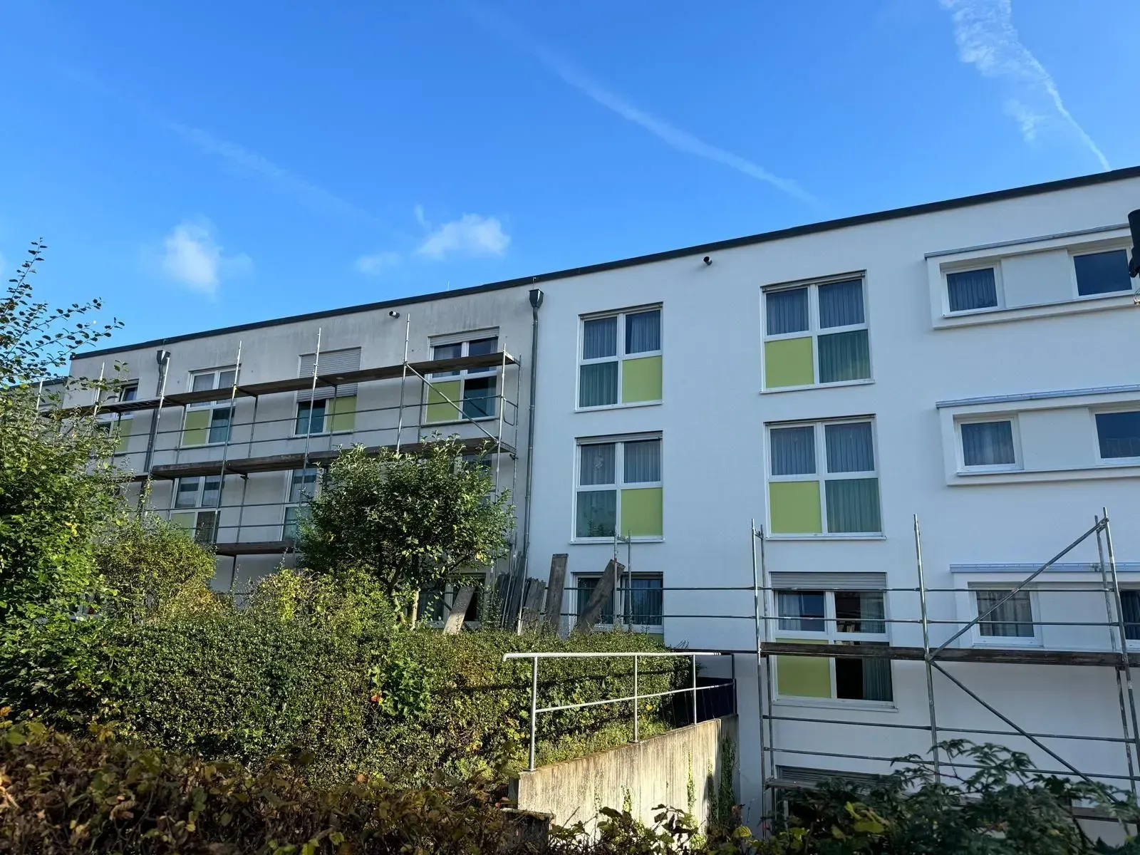 Modernes Wohnhaus mit Balkonen und weiß-grüner Fassade unter blauem Himmel