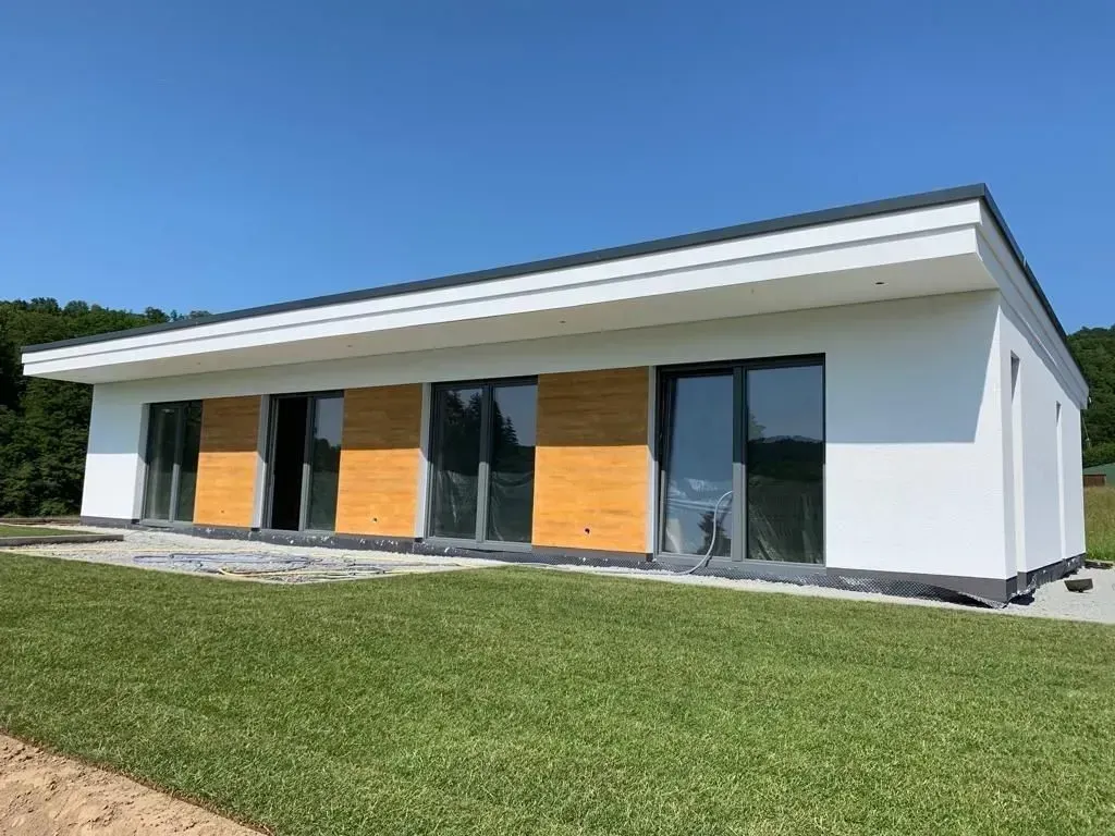 Modernes, weißes, eingeschossiges Haus mit orangefarbenen Fensterläden und einem Rasen