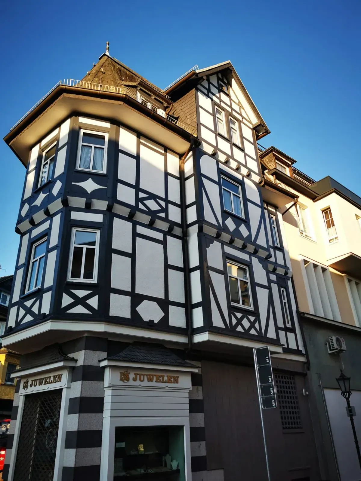 Eckgebäude aus Fachwerk mit weißen Wänden und dunklen Balken unter klarem, blauem Himmel