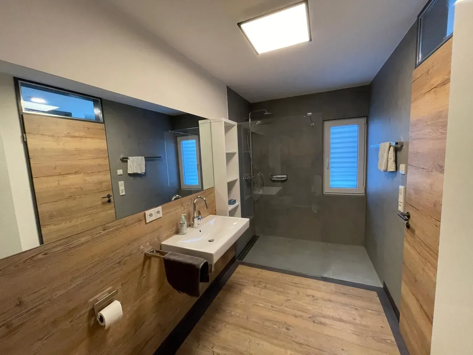 Modernes Badezimmer mit Holzelementen, Doppelwaschtisch und verglaster Dusche.