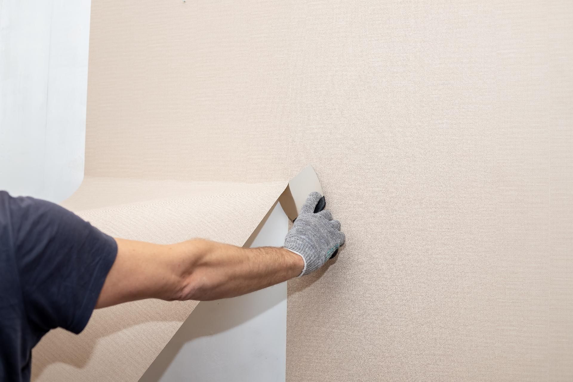Eine behandschuhte Hand trägt Wandputz auf eine beige, strukturierte Innenwand auf.