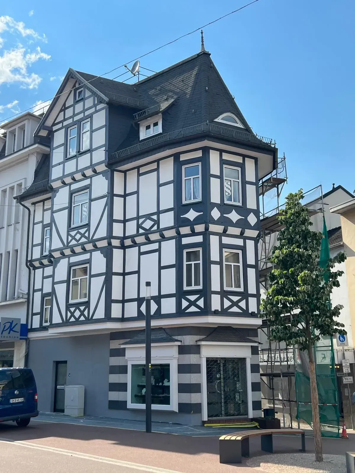 Weißes Fachwerkhaus mit dunklen Verzierungen an einer Straßenecke unter blauem Himmel