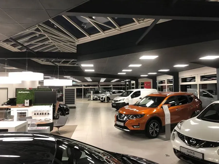 Autohaus mit mehreren Fahrzeugen, darunter orange und weiße Autos unter hellem Deckenlicht