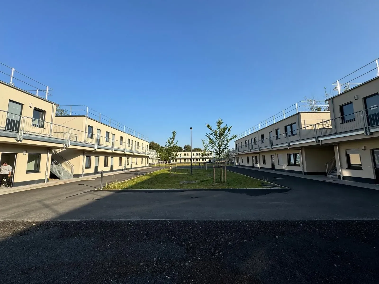 Symmetrischer Wohnhof mit beigefarbenen Gebäuden und einem zentralen Rasenstreifen unter klarem, blauem Himmel