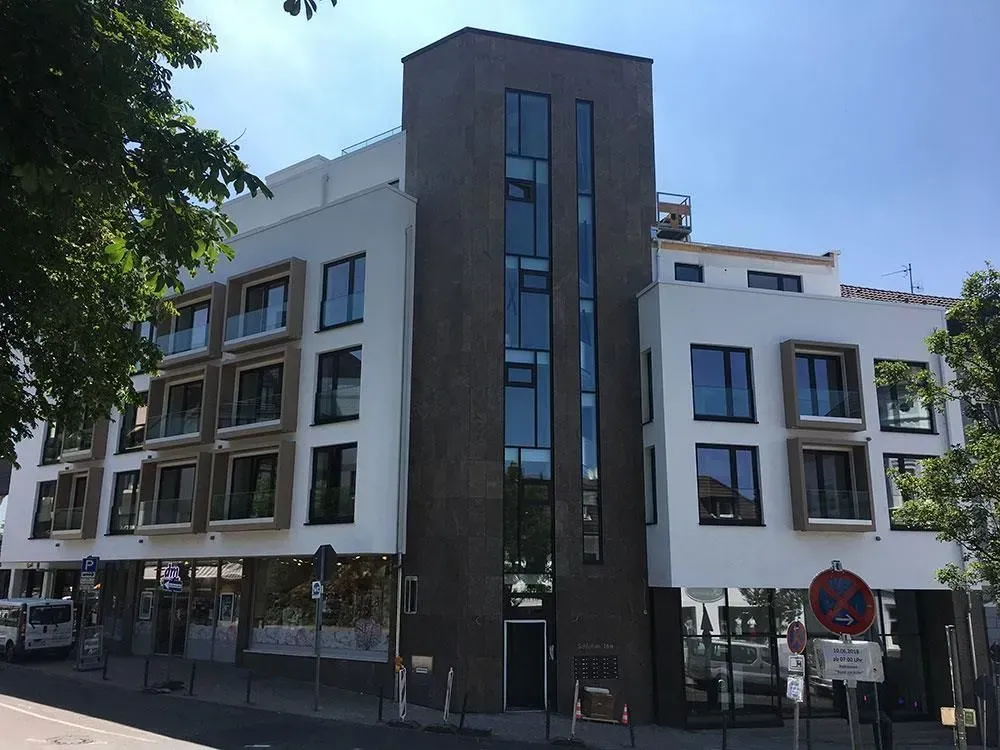 Modernes Wohnhaus mit weißen Fassaden, dunklem Mittelturm und Balkonen an einer Stadtstraße