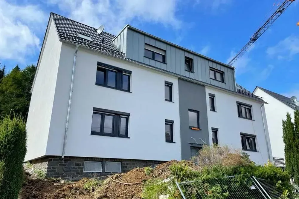 Modernes weißes Apartmentgebäude mit dunklen Fenstern an einem Hang unter blauem Himmel