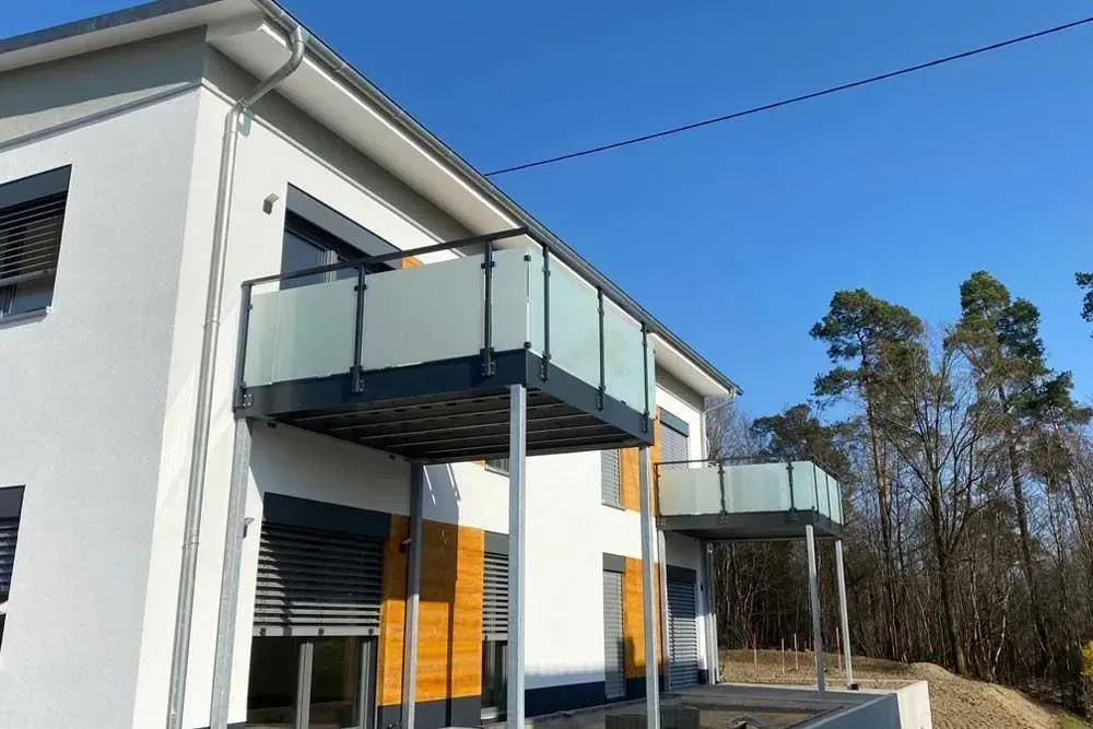 Modernes Haus mit Glasbalkonen und weißen Wänden unter klarem, blauem Himmel