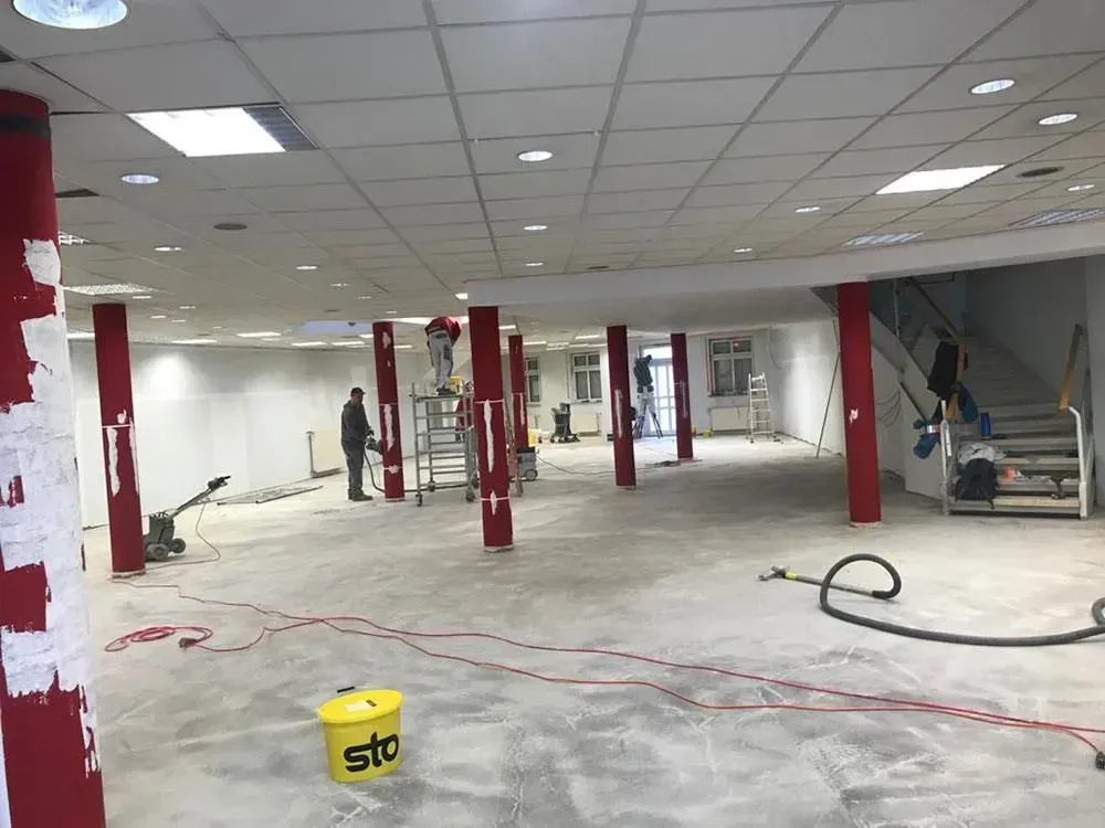 Leeres Büro im Umbau mit roten Stützsäulen, freiliegendem Fußboden, Deckenplatten und Baumaterialien